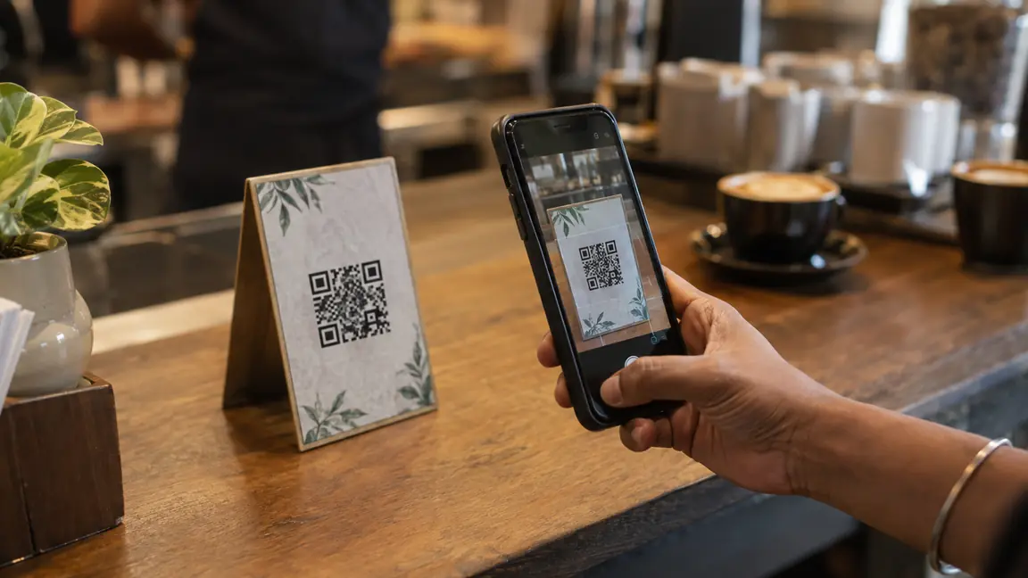 A phone scanning a printed QR code on a table tent at a cafe counter